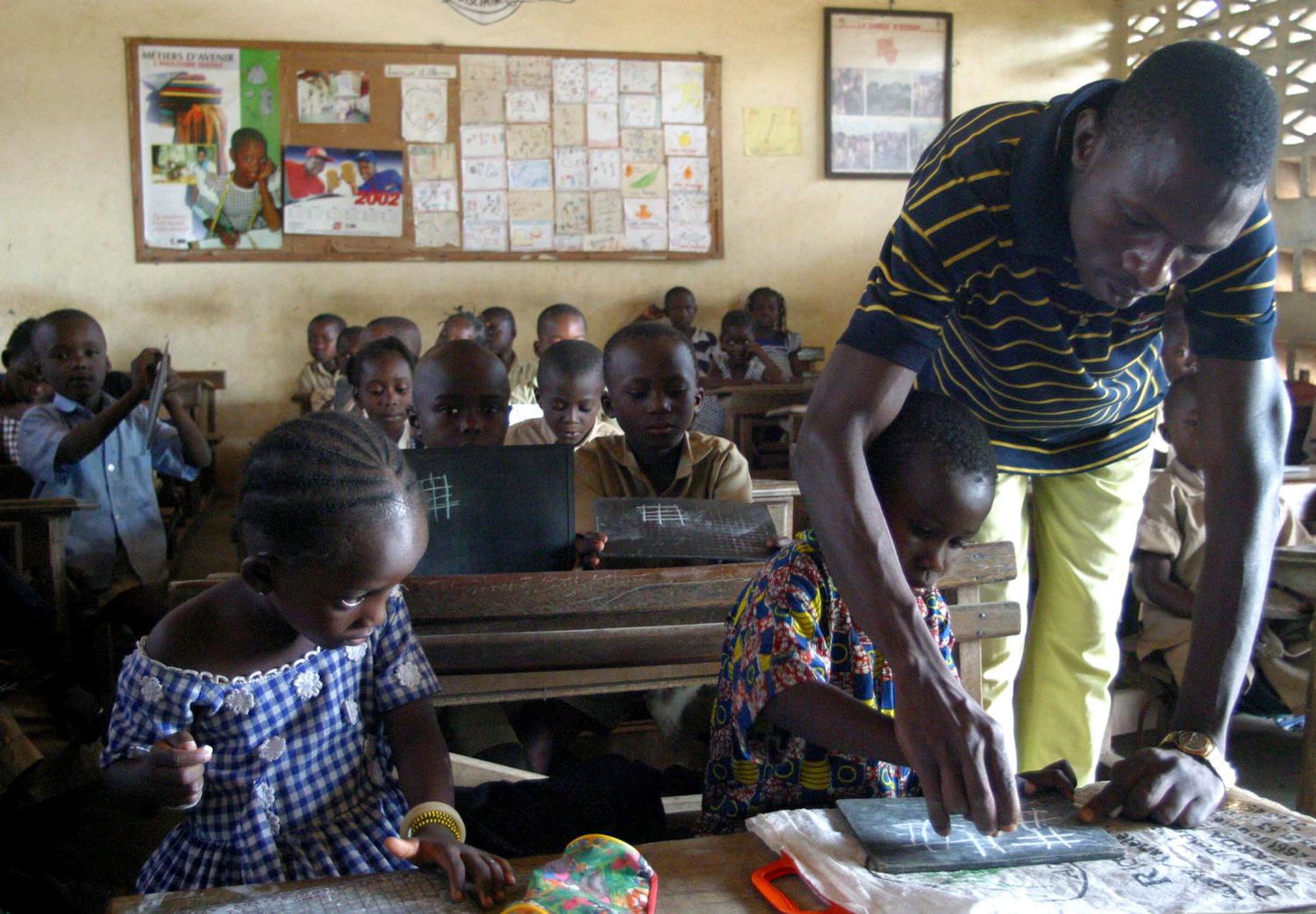 -PHOTO TAKEN  12JAN05- A teacher shows gives one of his early-year primary school pupils a hand with writing at a school in Bouake, January 12, 2005, [the stronghold of rebels holding the northern half of Ivory Coast since a civil war which erupted in 2002.] Headmistress Orokiatou Coulibalu's school has no doors and windows but it now has pupils and that gives thw quiet teacher with the thick glasses hope for the future in rebel-hald Ivory Coast. Picture taken on January 12, 2005.