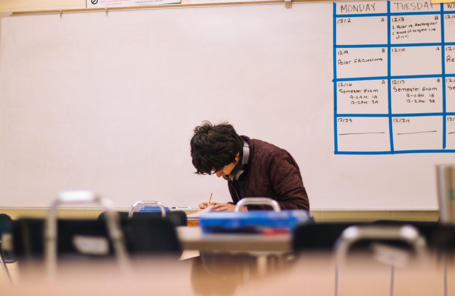 Male student working at desk in front of a whiteboard in a classroom.