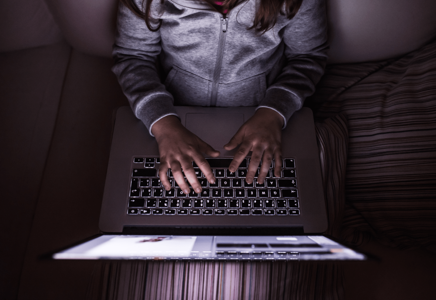 A top-down view of a person typing on a laptop in the dark.