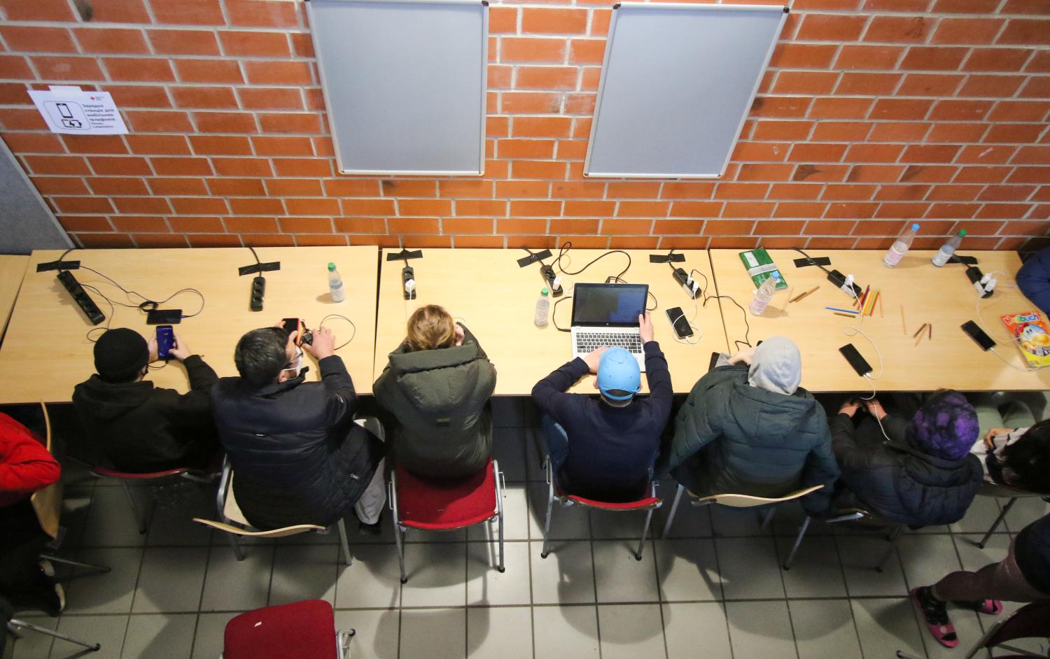 Refugees sit at a table and charge their cell phones at the emergency shelter for refugees from Ukraine in the Hessenhalle in Alsfeld.