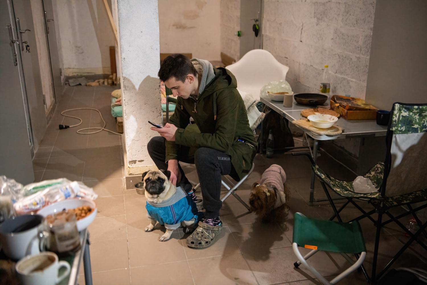 A man looks at his phone next to his two dogs in a basement near the blast that destroyed parts of a shopping mall in Kyiv.