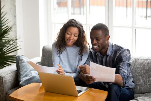 Married couple sitting on sofa at home read documents paper checking bills, bank account balance feeling satisfied and happy. Refund income last loan payment good news concept