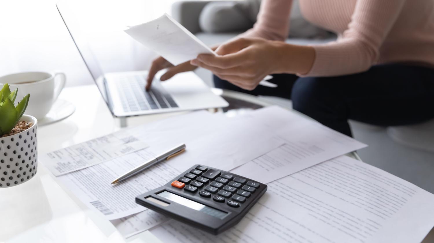 A calculator, paperwork, and computer on a table