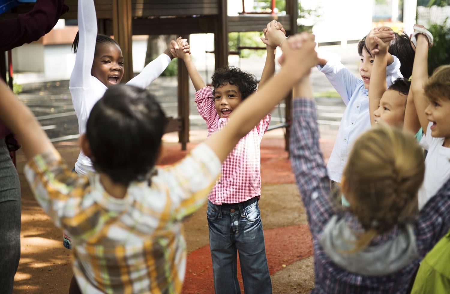 Group of diverse kindergarten students standing holding hands together.