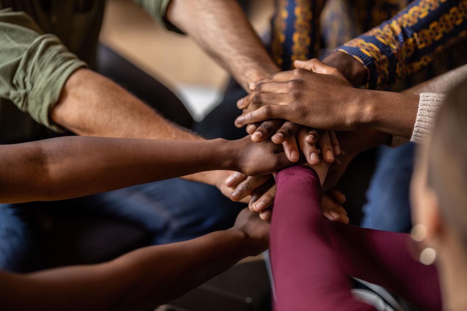 Cropped close of diverse businesspeople putting their hands on top of each other wearing casual clothes and African patterns.