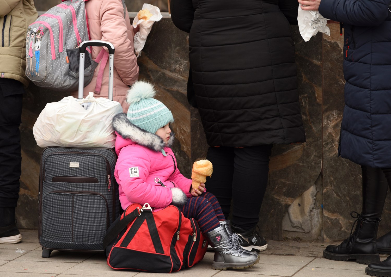 Ukrainian children sitting by suitcase after evacuating Eastern Ukraine.