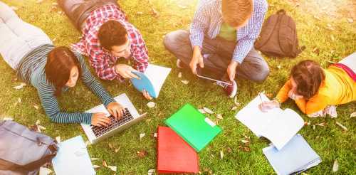 College,Students,Using,Laptop,While,Doing,Homework,At,Park