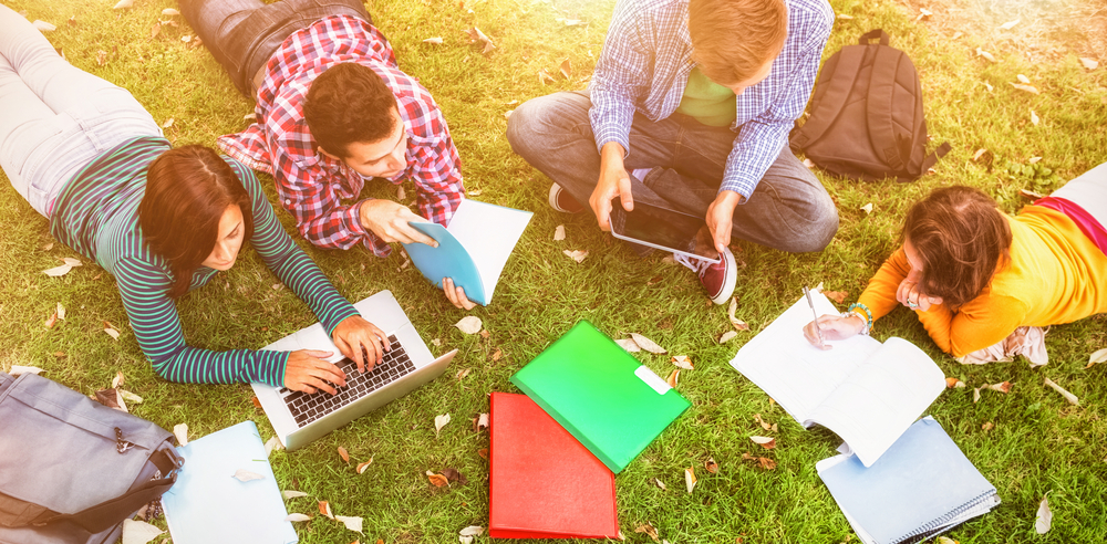 College,Students,Using,Laptop,While,Doing,Homework,At,Park