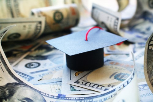 A graduation cap sits on a pile of $100 bills.