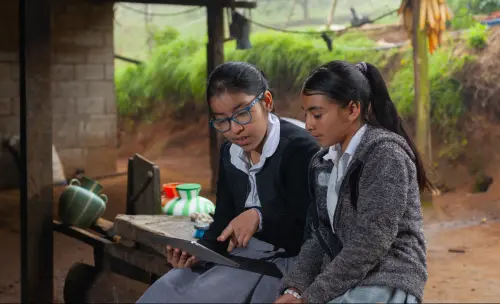 Two Colombian girl students doing their homework with a digital tablet at home.