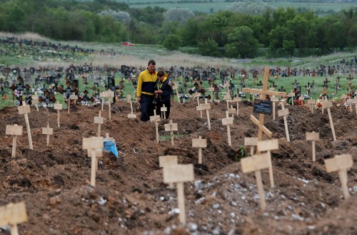People stand amid newly-made graves at a cemetery in the course of Ukraine-Russia conflict in the settlement of Staryi Krym outside Mariupol, Ukraine May 22, 2022. REUTERS/Alexander Ermochenko