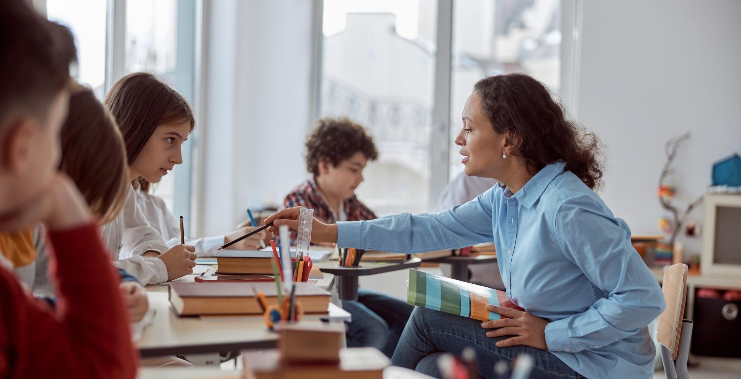 Female teacher helps students reading in classroom