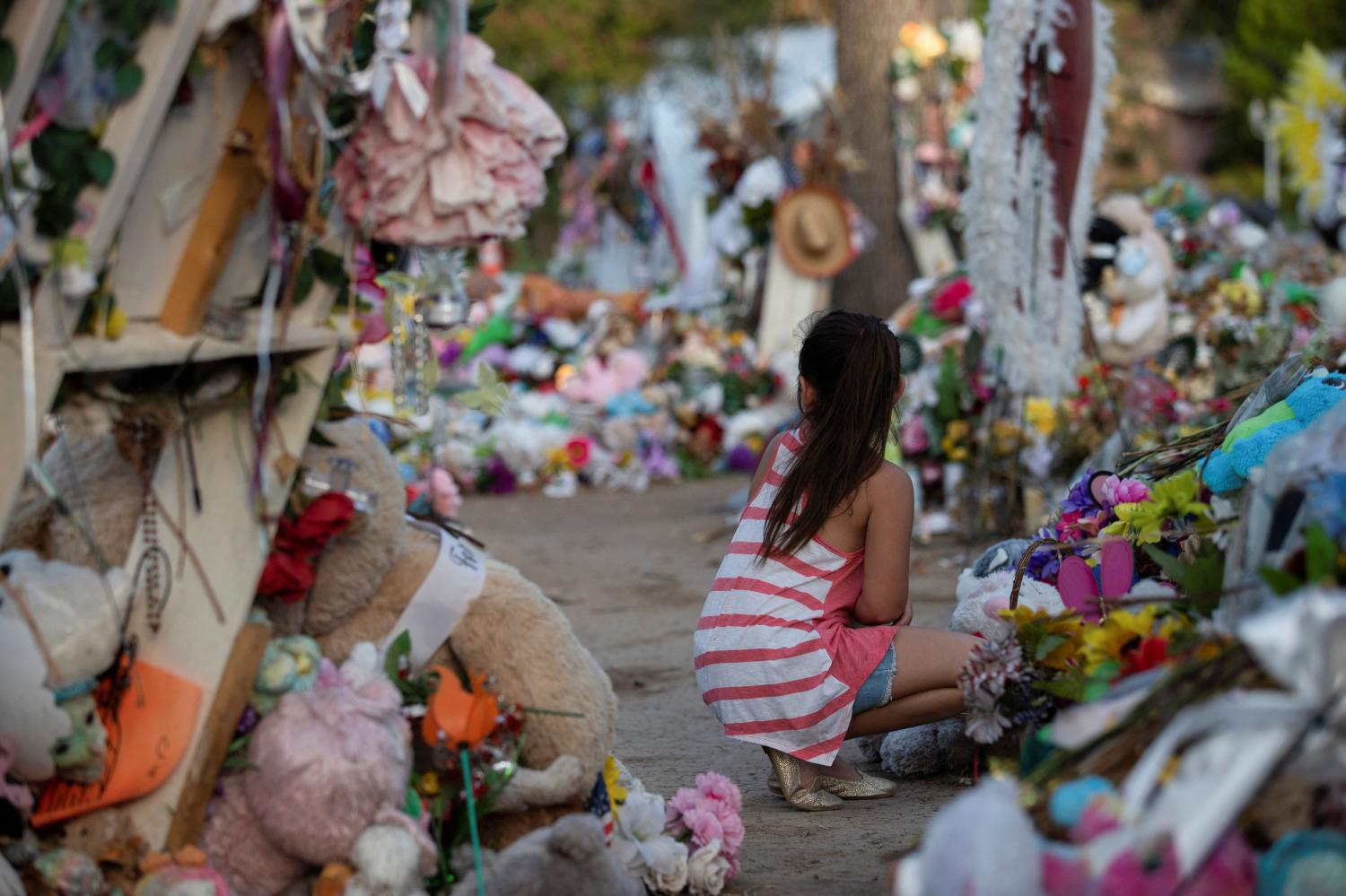 A girl sits at a memorial outside Robb Elementary School the day after video was released showing the May shooting inside the school in Uvalde, Texas, U.S., July 13, 2022