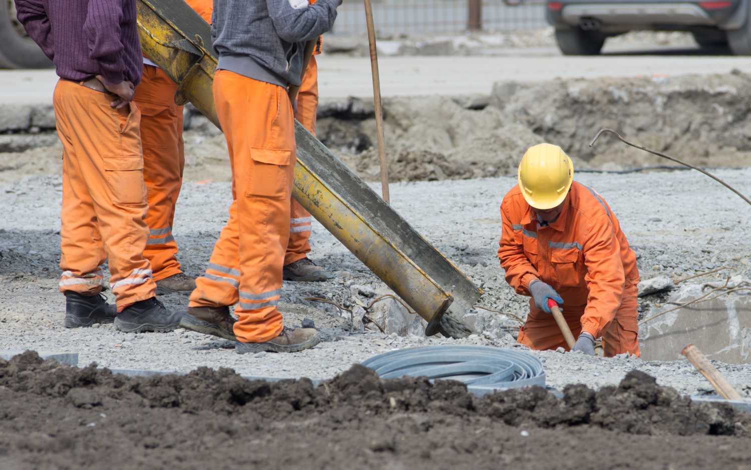 Worker leveling concrete poured from mixer on construction site