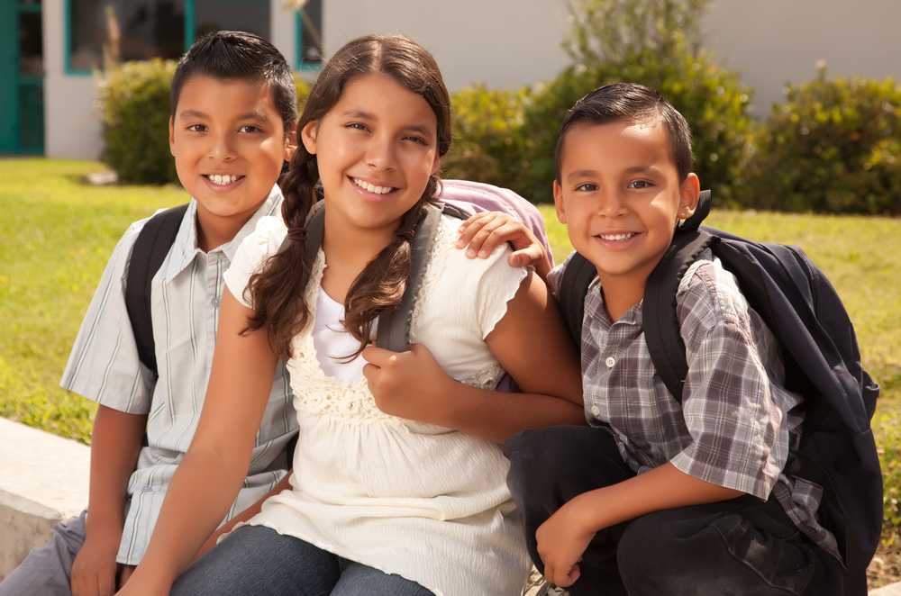 three young Latino students smiling outside of school