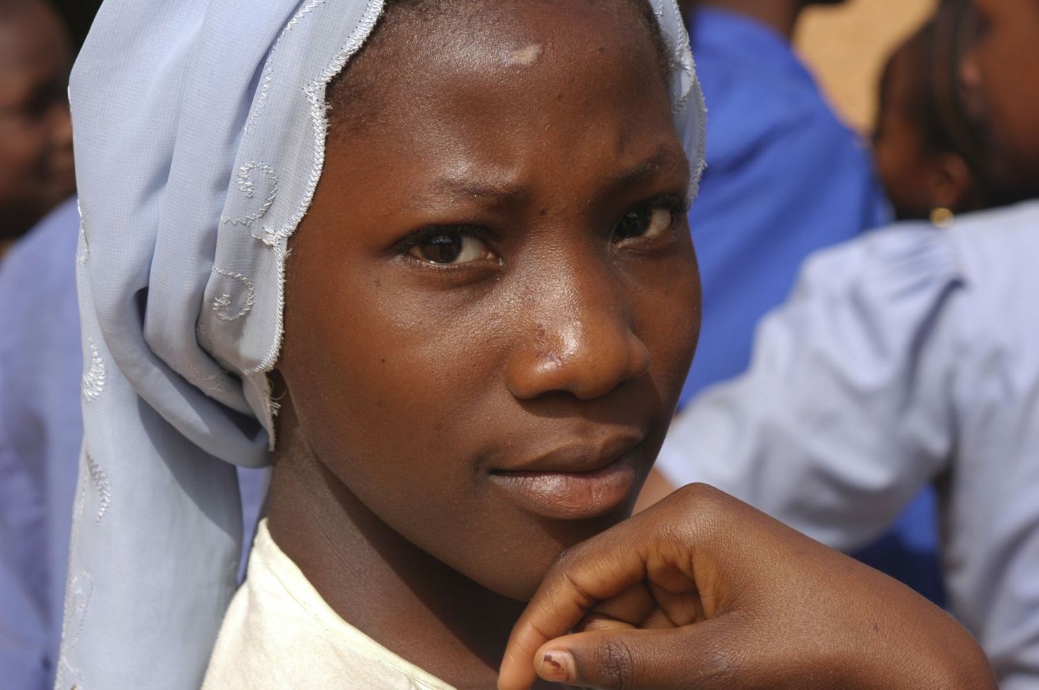 CIRCA 2009 Niger, Niamey, Portrait of an african muslim schoolgirl with a blue scarf covering her hair, and holding her hand before her mouth.