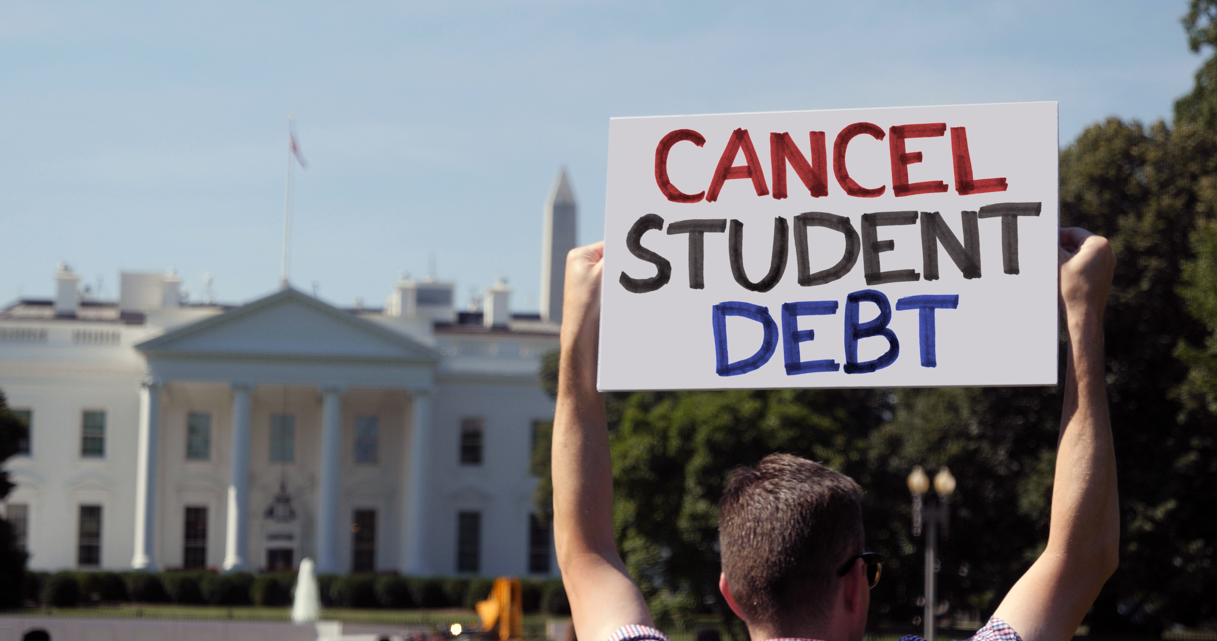 A man holds a cancel student debt sign in front of the White House