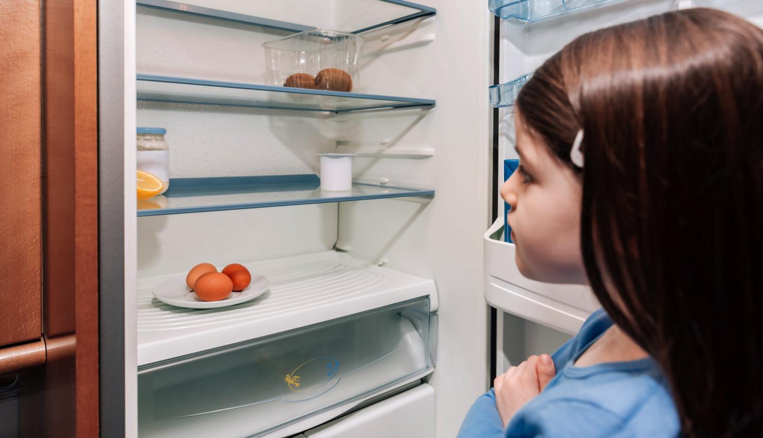 Girl looks into almost empty fridge