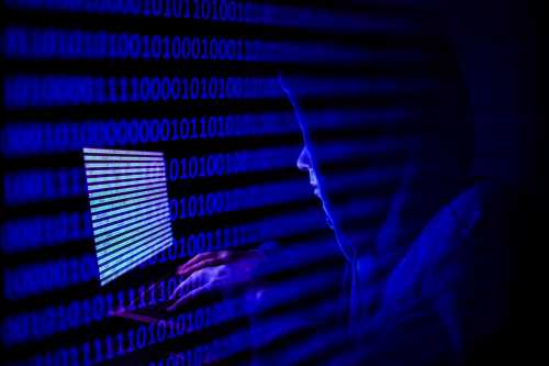 A person dressed as an internet hacker is seen with binary code displayed on a laptop screen in this double exposure illustration photo taken in Krakow, Poland on August 17, 2021. (Photo by Jakub Porzycki/NurPhoto)NO USE FRANCE