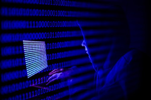 A person dressed as an internet hacker is seen with binary code displayed on a laptop screen in this double exposure illustration photo taken in Krakow, Poland on August 17, 2021. (Photo by Jakub Porzycki/NurPhoto)NO USE FRANCE