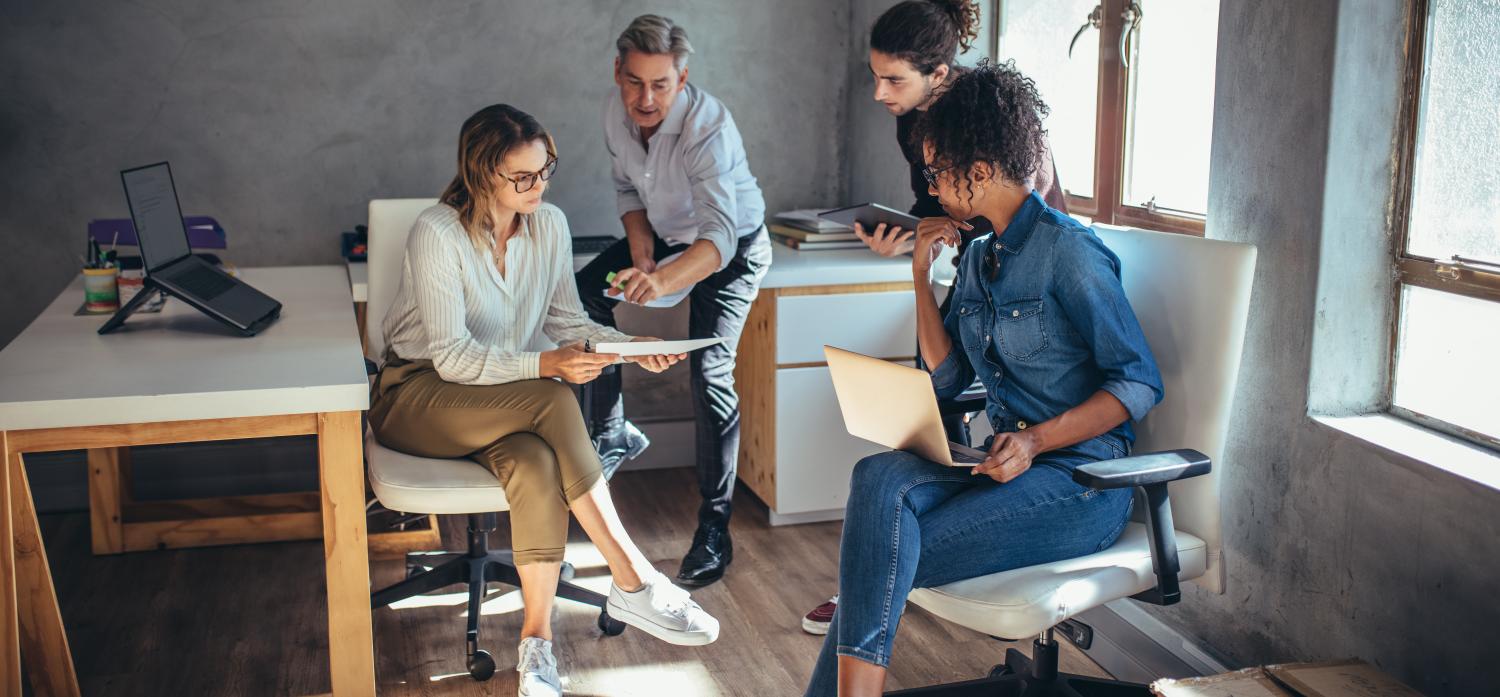 Diverse group of business people working together at a small office. Woman showing her digital tablet and discussing new business plan with coworkers.