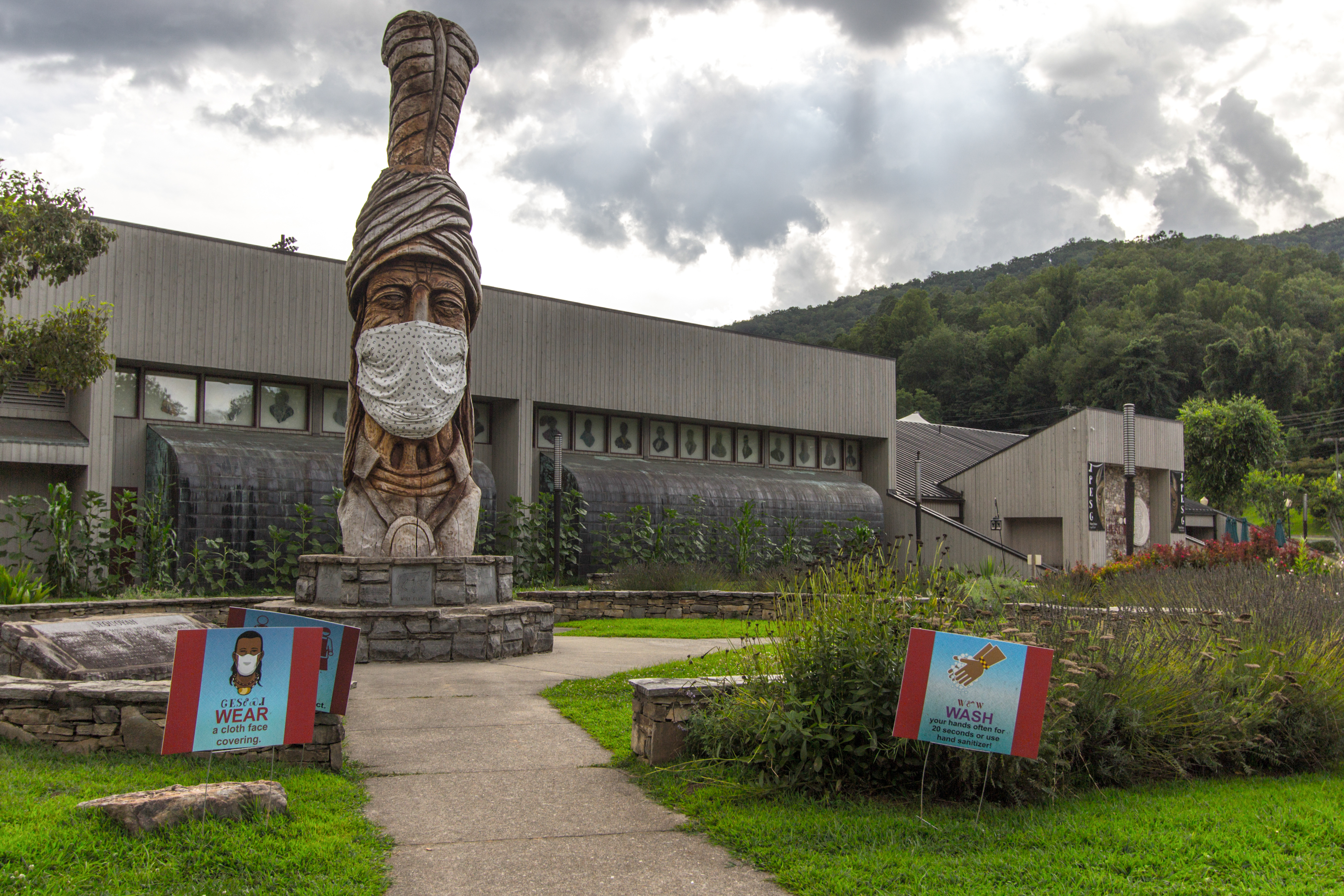 Cherokee, North Carolina, USA - August 12, 2020: Large Totem Pole outside of the Museum of the Cherokee Indian with a face mask and signs for mask requirement to slow the spread of COVID-19.