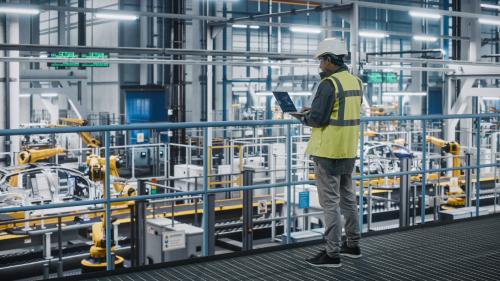 Car factory engineer in high visibility vest using laptop computer