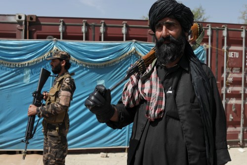 Taliban fighters stand guard while people wait to receive sacks of rice, as part of humanitarian aid sent by China to Afghanistan, at a distribution centre in Kabul, Afghanistan, April 7, 2022. REUTERS/Ali Khara