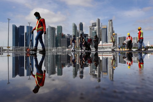 Migrant workers conduct checks on a road surface with the city skyline pictured in the background at Marina Bay on February 13, 2022 in Singapore. (Photo by Suhaimi Abdullah/NurPhoto)NO USE FRANCE