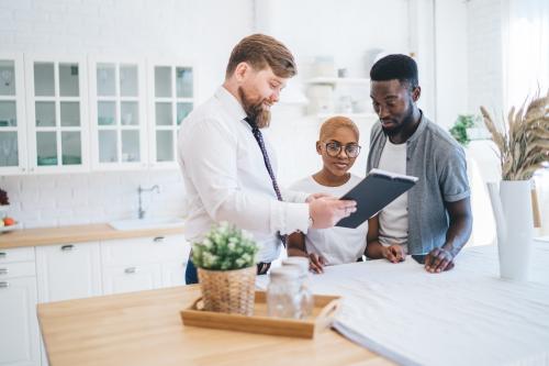 Photo of a white realtor showing a Black couple information about their house.