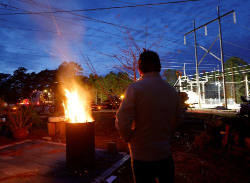 Gerardo Anicero warms himself in front of a makeshift fire as he watches Duke Energy personnel work to restore power at a crippled electrical substation that the workers said was hit by gunfire after the Moore County Sheriff said that vandalism caused a mass power outage, in Carthage, North Carolina, U.S. December 4, 2022.  REUTERS/Jonathan Drake