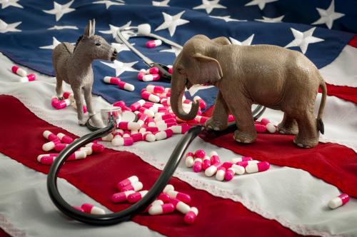 Toy elephant and donkey standing on American flag with pills between them.