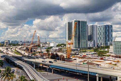 Miami, Florida, USA - September 25th, 2021 - Downtown overlooking highway construction traffic, buildings and cranes on 395 MacArthur Causeway toward everglades into dark cumulus nimbus storm clouds