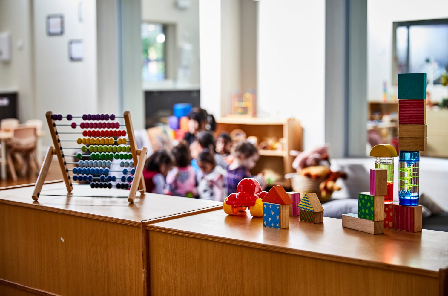 Interior photography detail of toys and educational equipment in a childcare center with preschoolers out of focus in the background