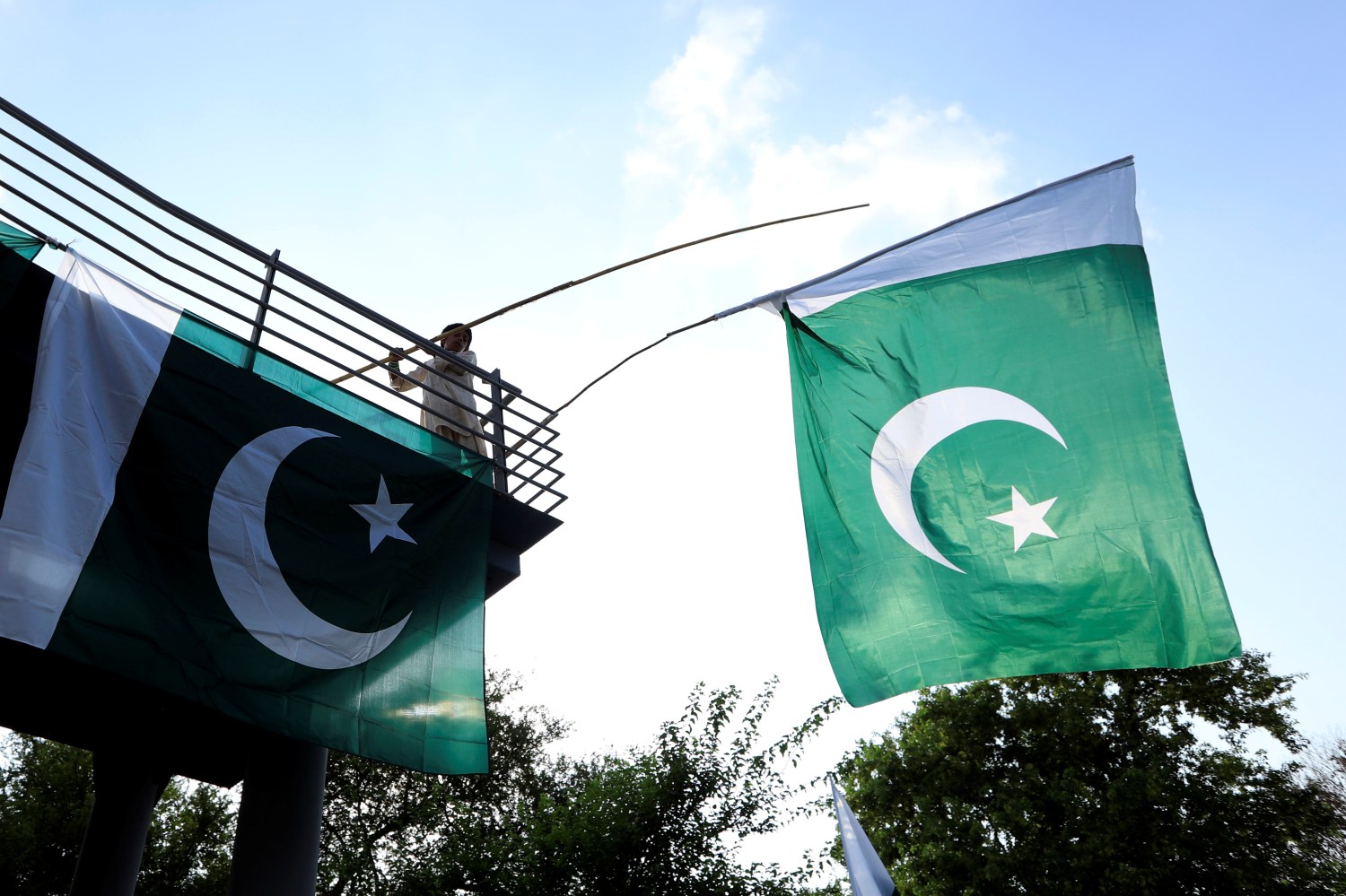 FILE PHOTO: A boy uses a bamboo stick to adjust national flags at an overhead bridge ahead of Pakistan's Independence Day, in Islamabad, Pakistan August 10, 2018. REUTERS/Faisal Mahmood