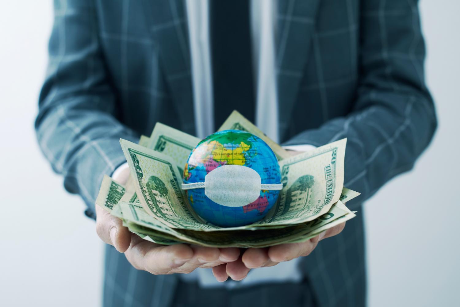 Man holding money and globe with surgical mask.