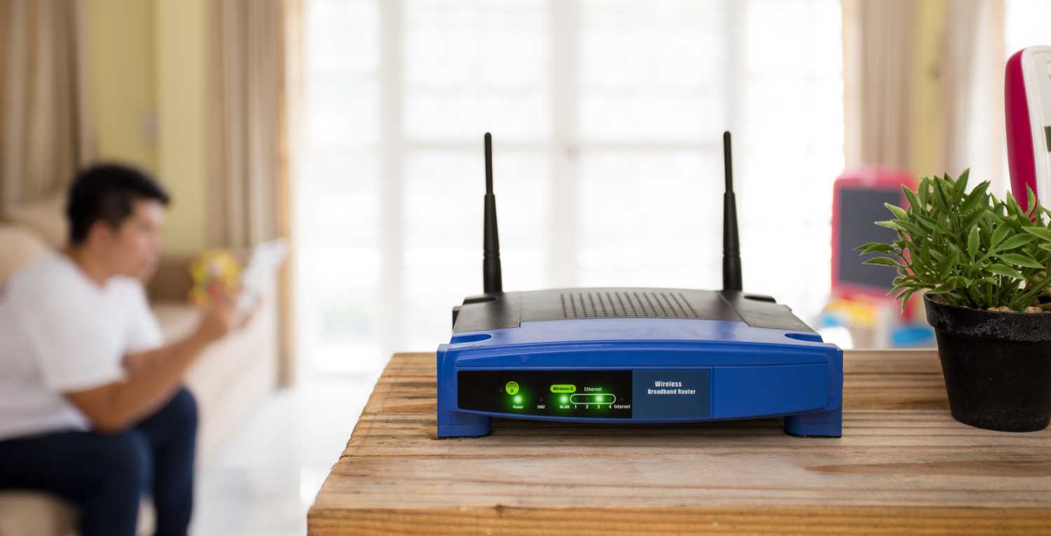 closeup of a wireless router and a young man using Tablet on living room at home with a window in the background