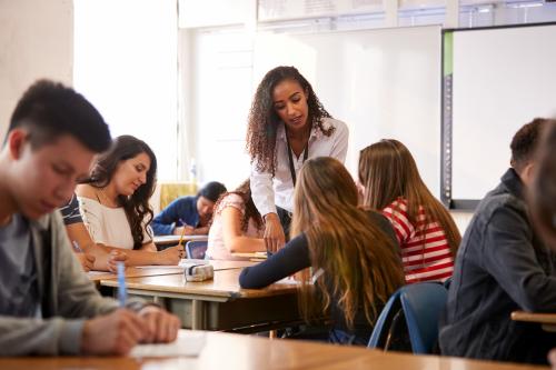 Female,High,School,Teacher,Standing,By,Student,Table,Teaching,Lesson
