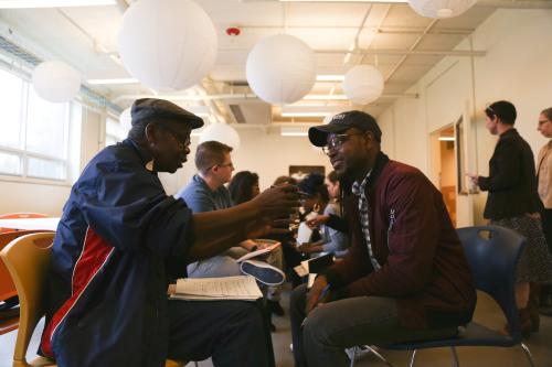 An older man and younger man having a conversion inside a classroom setting. Older man is taking notes in a notebook. Drexel University. Photo: Courtesy of Writers Room