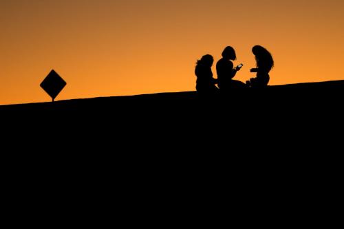 Young girls look at their phones as they sit on a hillside after sun set in El Paso, Texas, U.S., June 20, 2018. REUTERS/Mike Blake