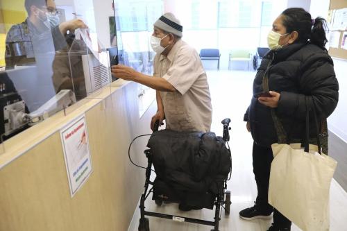 Ananias Ocampo receives paperwork following an appointment with a dermatologist at Cook County Health on March 14, 2022. At right is advocate and caregiver Hilda Burgos. Ocampo, 78, has health insurance thanks to the Medicaid-like program that now benefits immigrants 65 and older regardless of their immigration status.No Use undefined ** CHICAGO.