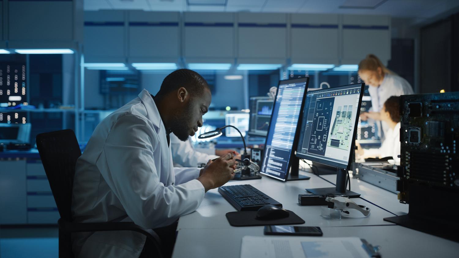 Modern Electronics Development Facility: Black Engineer and Diverse Team of Multi-Ethnic Scientists Work on Computers, Design Industrial PCB, New Generation Silicon Microchips, Semiconductors Photo: Shutterstock