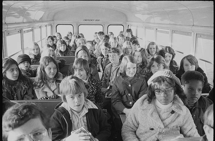 A school bus with children wearing coats, seated three across.