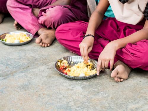 PUDUCHERRY, TAMIL NADU, INDIA - DECEMBER Circa, 2018. Unidentified poor classmates children with uniforms sitting on the floor outdoors, eating with their right hand some rice with masala.