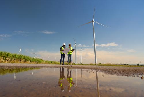 Male an Female colleague read drawing work at out door of Wind turbine farm, Green energy and renewal energy concept