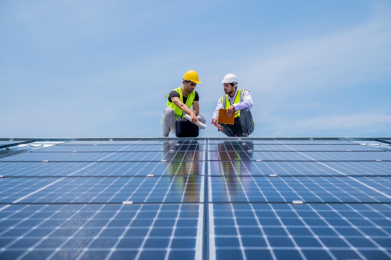 Engineer talking about solar system installation on roof in sunny day with blue sky, using clean and green power energy in industrial level concept.