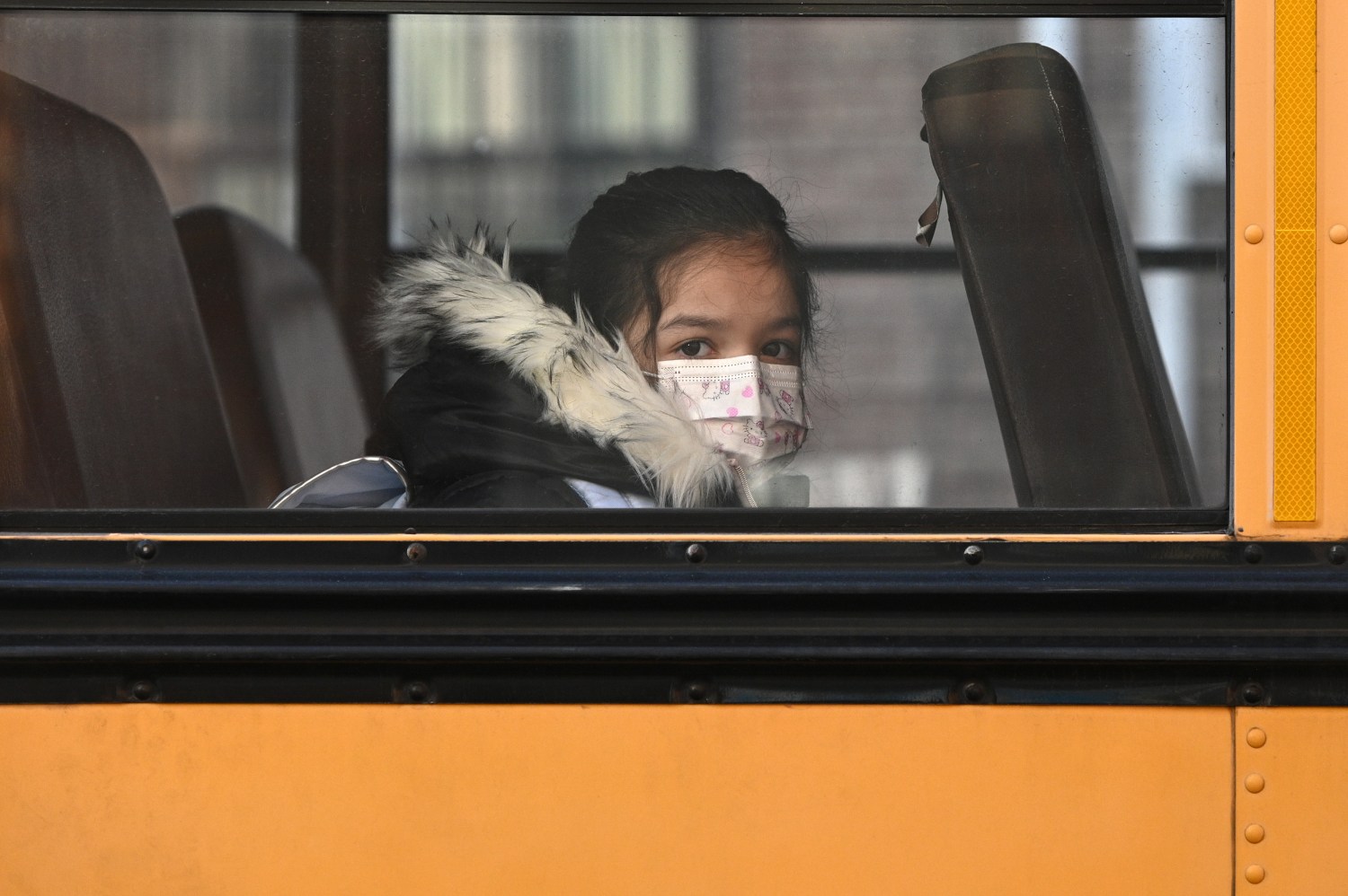 A student on a school bus wears a mask as she arrives at P.S. 7 Louis F. Simeone as the masks policy for K through 12 is lifted, Queens, New York, NY, March 7, 2022.