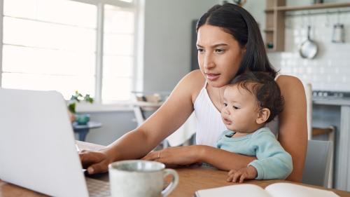 A mother works remotely with her child on her lap
