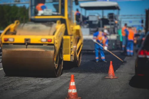 Process of asphalting and paving, asphalt paver machine and steam road roller during road construction and repairing works, workers working on the new road construction site, placing a layer in summer