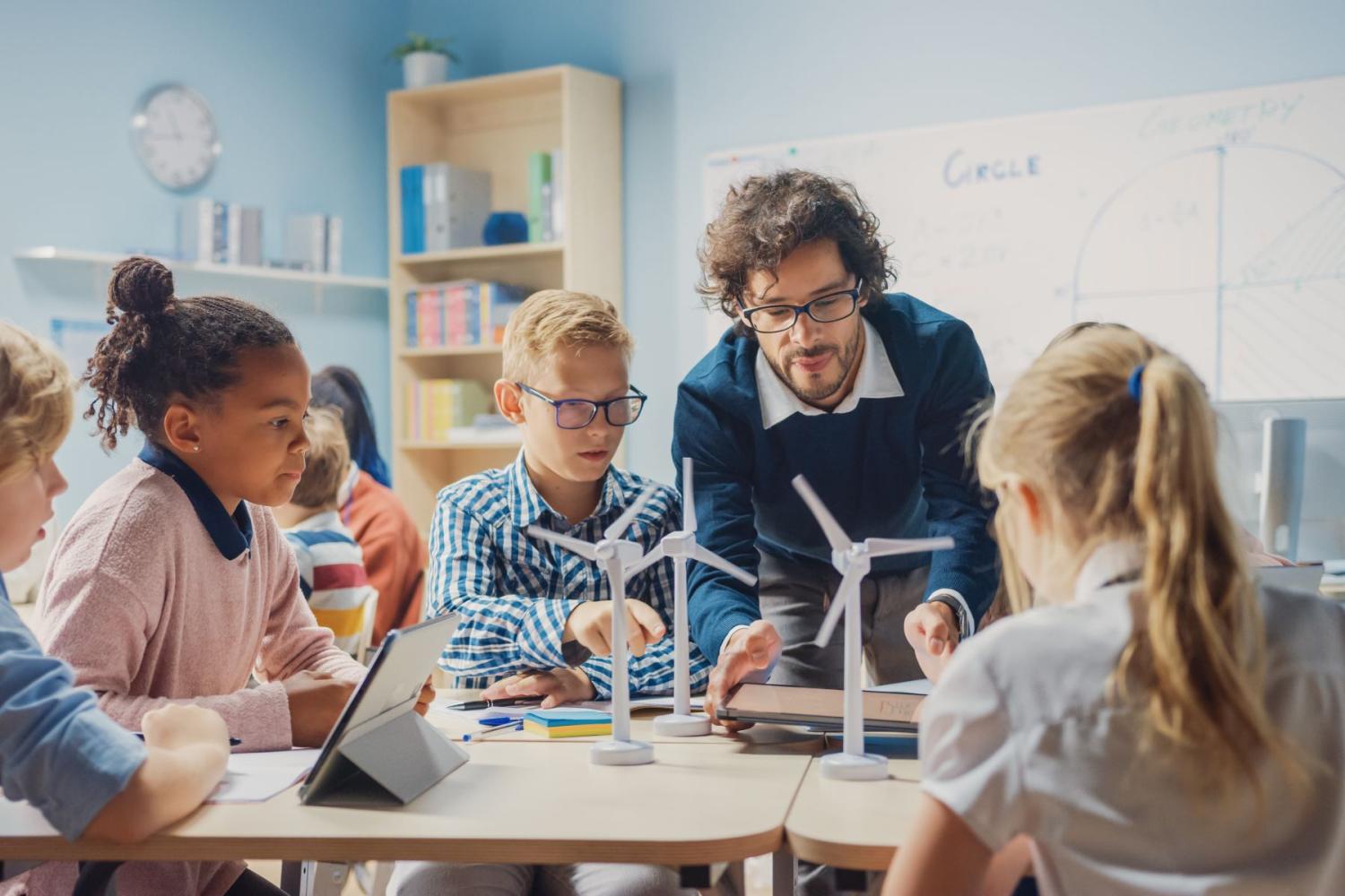 A teacher and elementary school students examine a model windmill in the classroom.